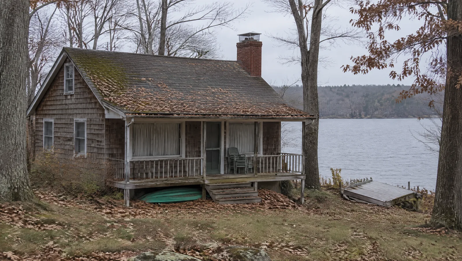 Closed-up lake cottage with a capped brick chimney and fallen leaves on the roof