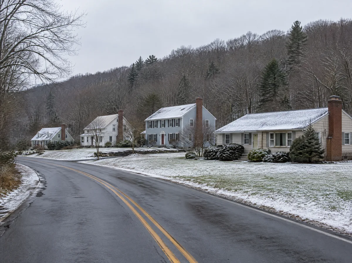 Modest homes with brick chimneys along a wooded country road after the first light snow